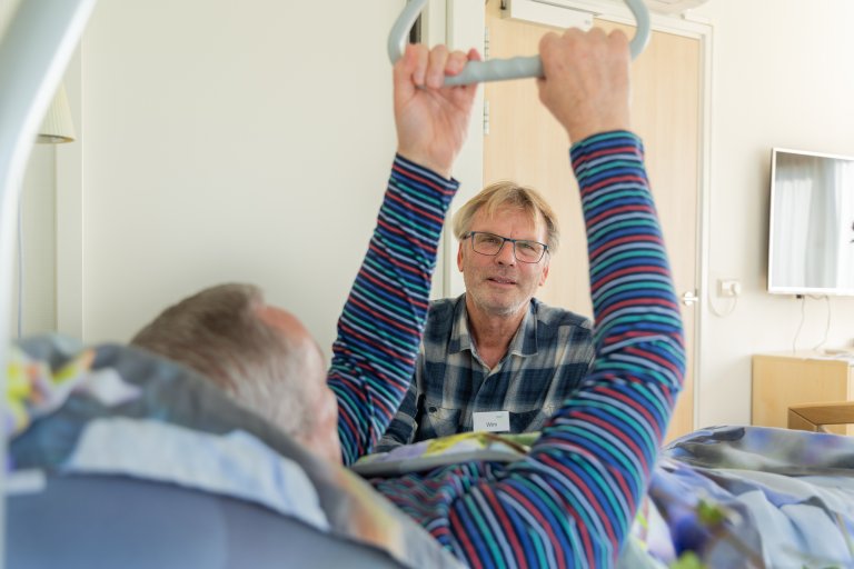 Foto van een vrijwilliger naast het bed van een gast
